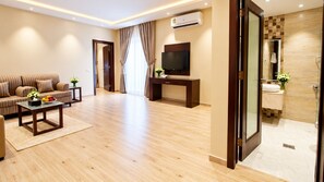 A modern living room with a sofa, coffee table, and TV. There is a bathroom with a shower and sink. - Al Muhaidb Residence Sudair - Economic (Al Majmaah)
