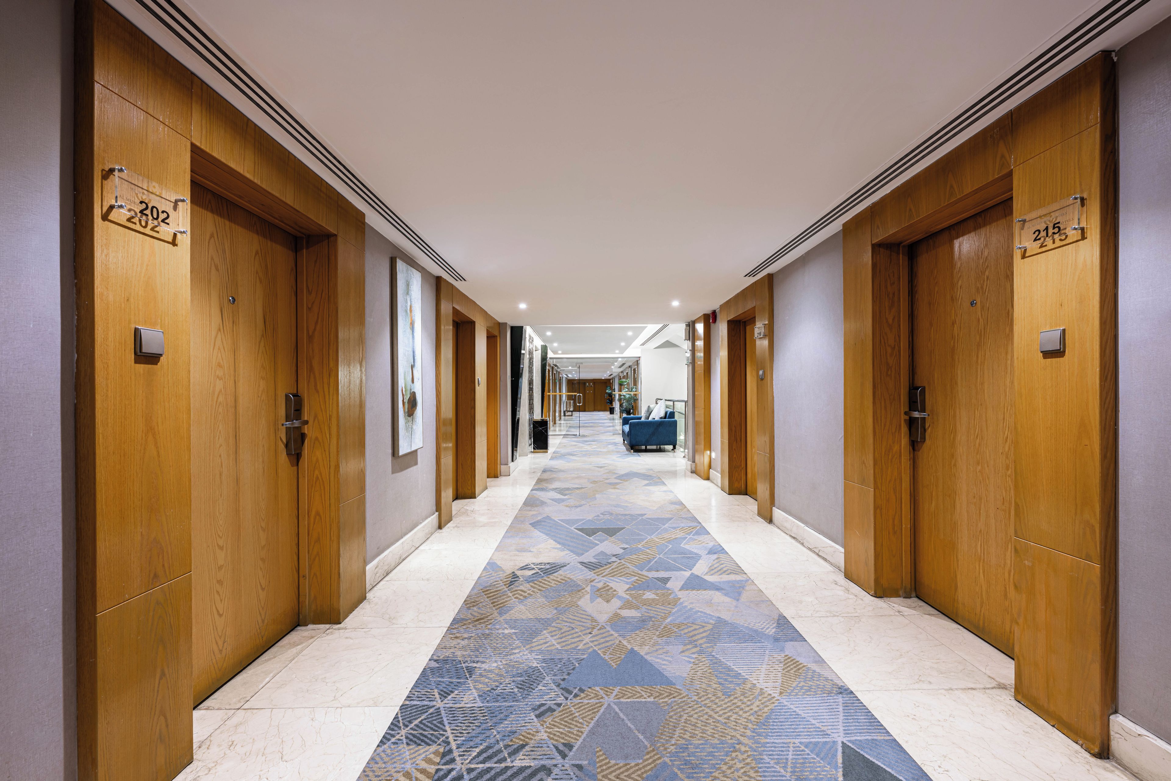 A hotel corridor with wooden doors, numbered room signs, and a patterned carpet.