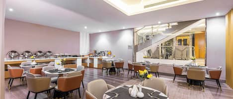 Un área de comedor de hotel moderna con varias mesas y sillas, un bar y una escalera que lleva a un nivel superior.