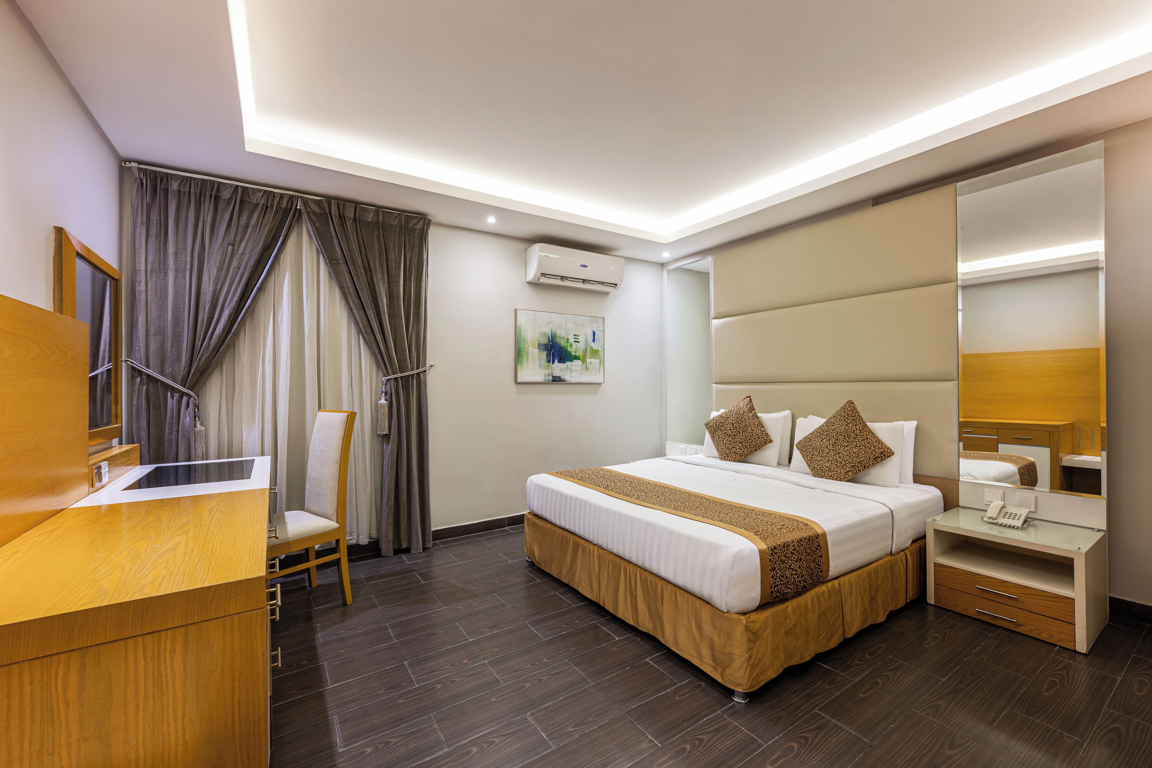 Habitación de hotel moderna con una cama, un escritorio, una silla, un equipo de aire acondicionado y un espejo grande.