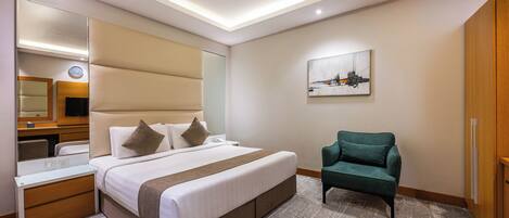 A hotel room with a bed, bedside table, chair, artwork, and a mirror.