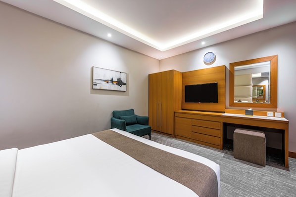 A hotel room with a bed, a desk with a flat-screen TV, a chair, a wardrobe, and a large mirror.