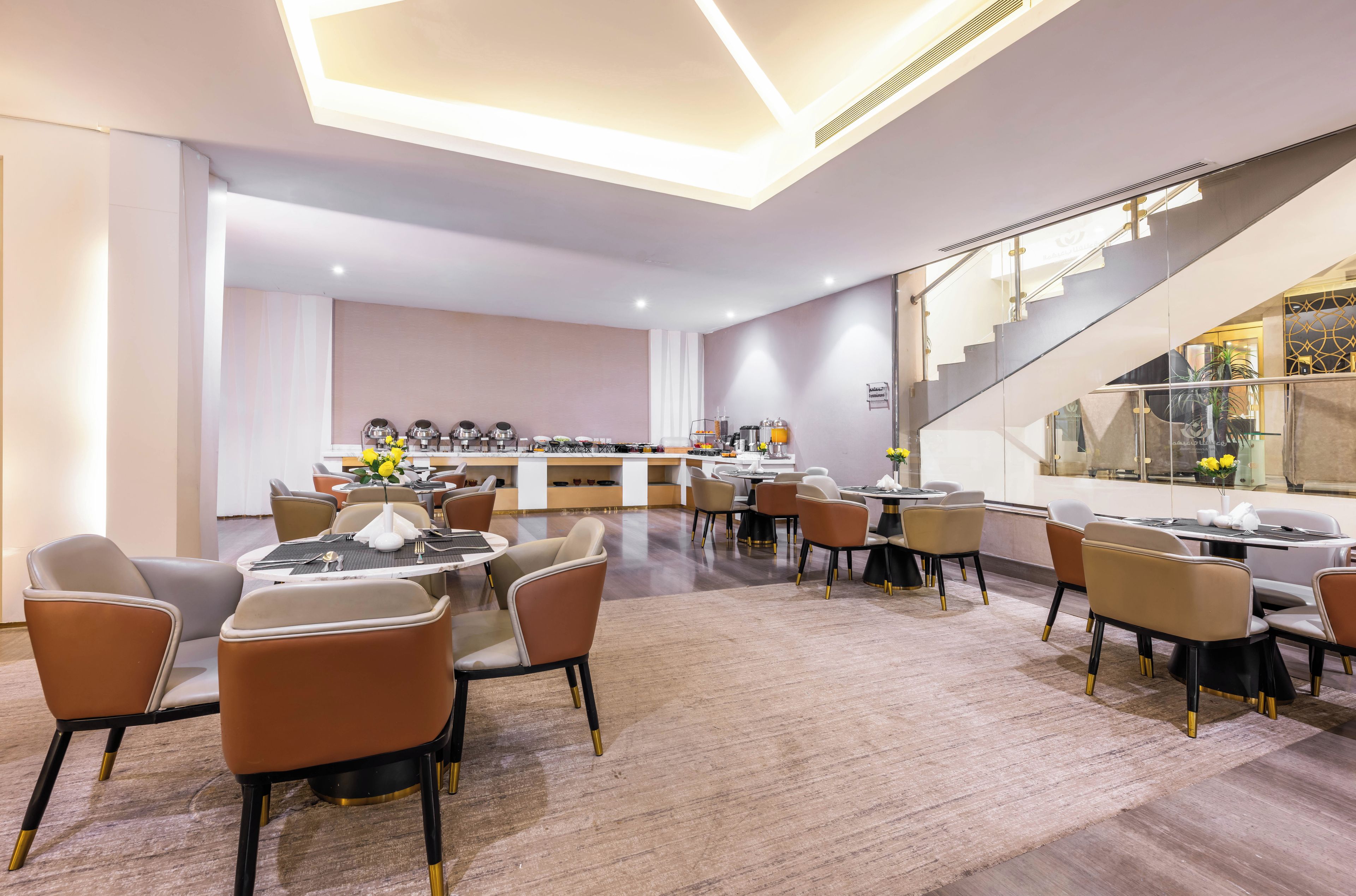 Een moderne hotellobby met een bar in het midden, verschillende zithoeken en een trap naar een hoger niveau.