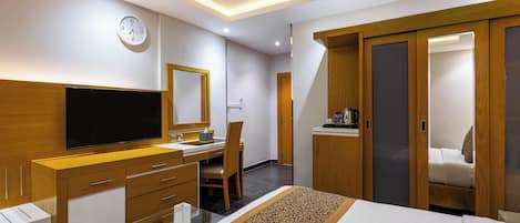 A hotel room with a bed, a desk with a flat-screen TV, a wardrobe, and a bathroom door.