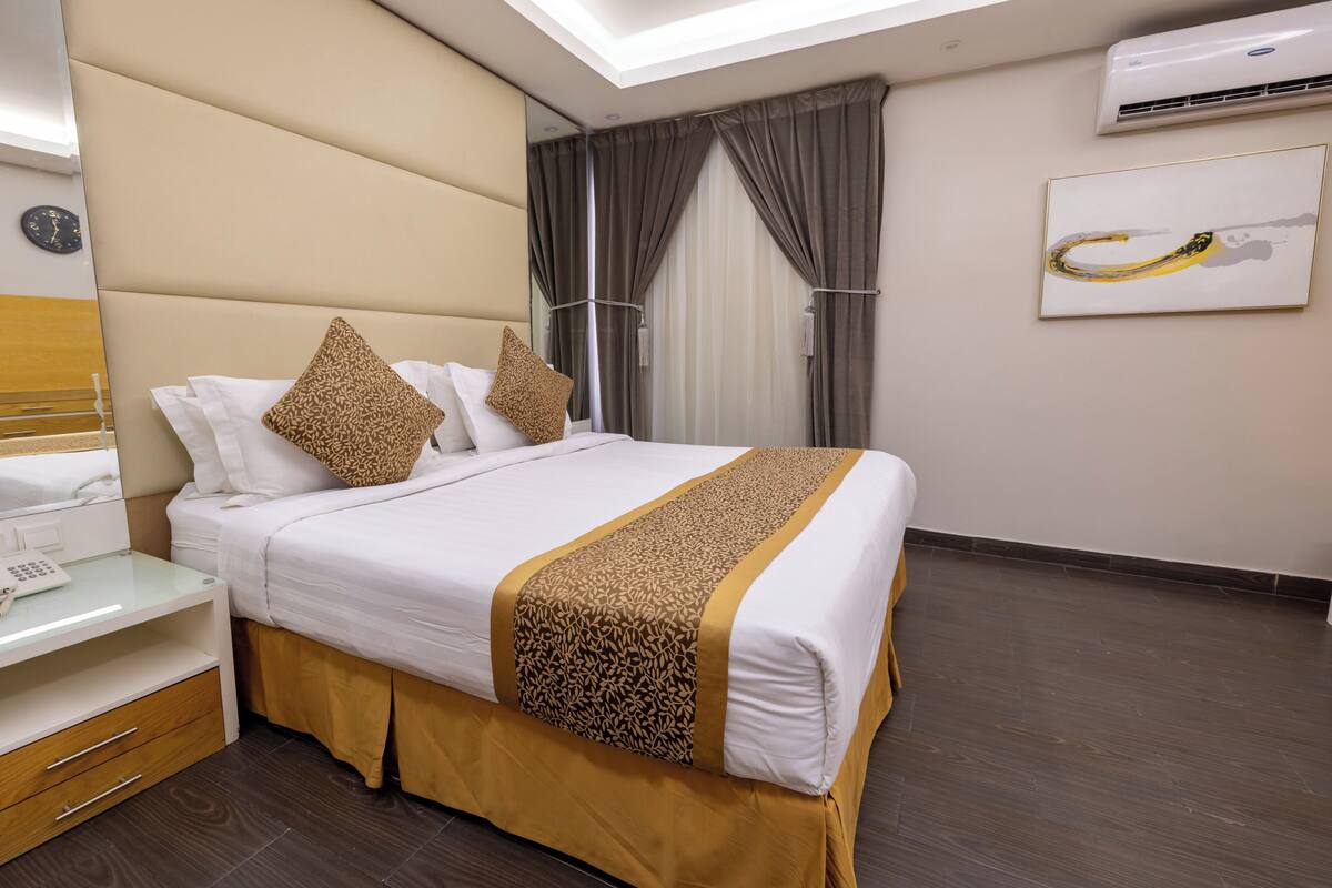 A hotel room with a bed, bedside table, and a wall-mounted air conditioner.