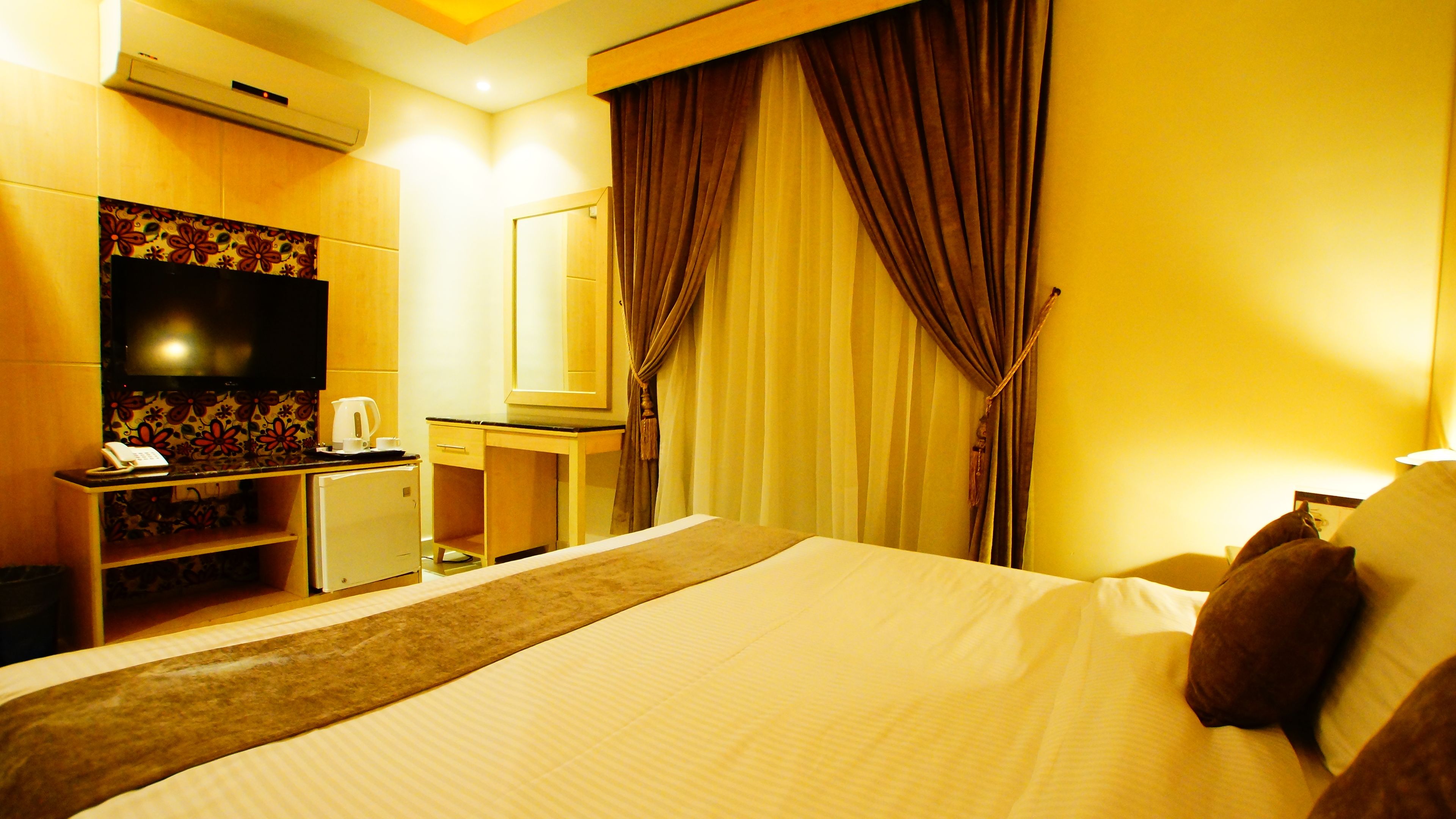 Une chambre d’hôtel avec un lit, un bureau avec un téléphone, une télévision et des rideaux.