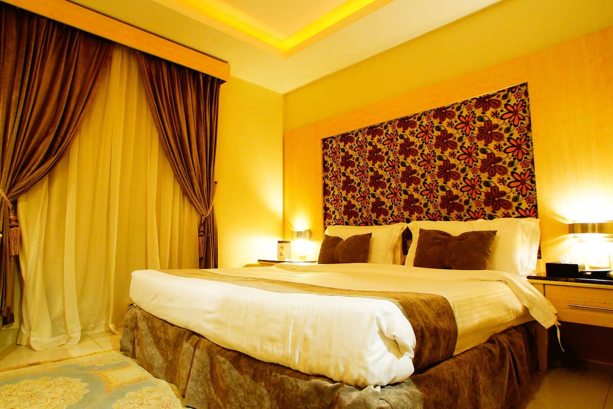 Ein Hotelzimmer mit einem großen Bett, zwei Nachttischen, einem Spiegel und einem blumengemusterten Kopfteil.