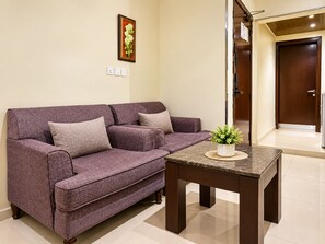 A purple sofa with two cushions, a small table with a plant, and a door in the background.