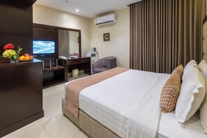 Quarto de hotel com cama, escrivaninha, televisão, ar condicionado e janela com cortinas.