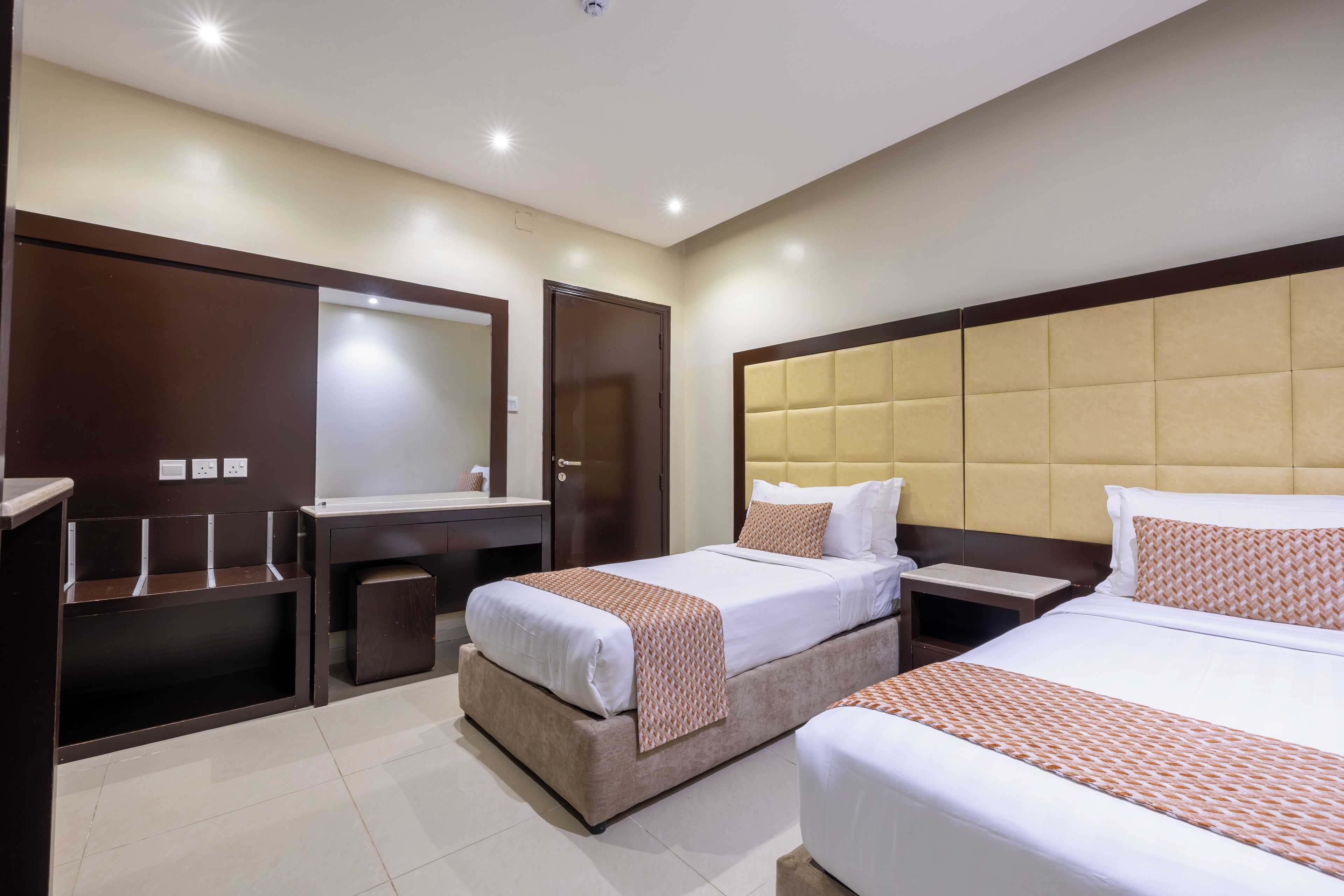 Une chambre d’hôtel avec deux lits, un grand miroir, une coiffeuse avec un lavabo et une petite poubelle.