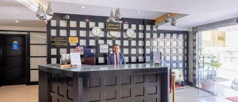A reception desk with a clock, a sign indicating a disabled room, and a reception area with a glass partition.