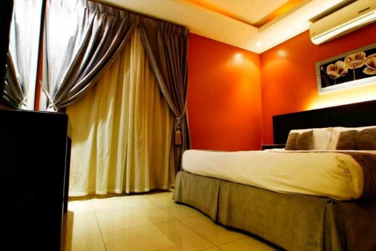 A hotel room with a bed, curtains, an air conditioning unit, and a wall-mounted picture.