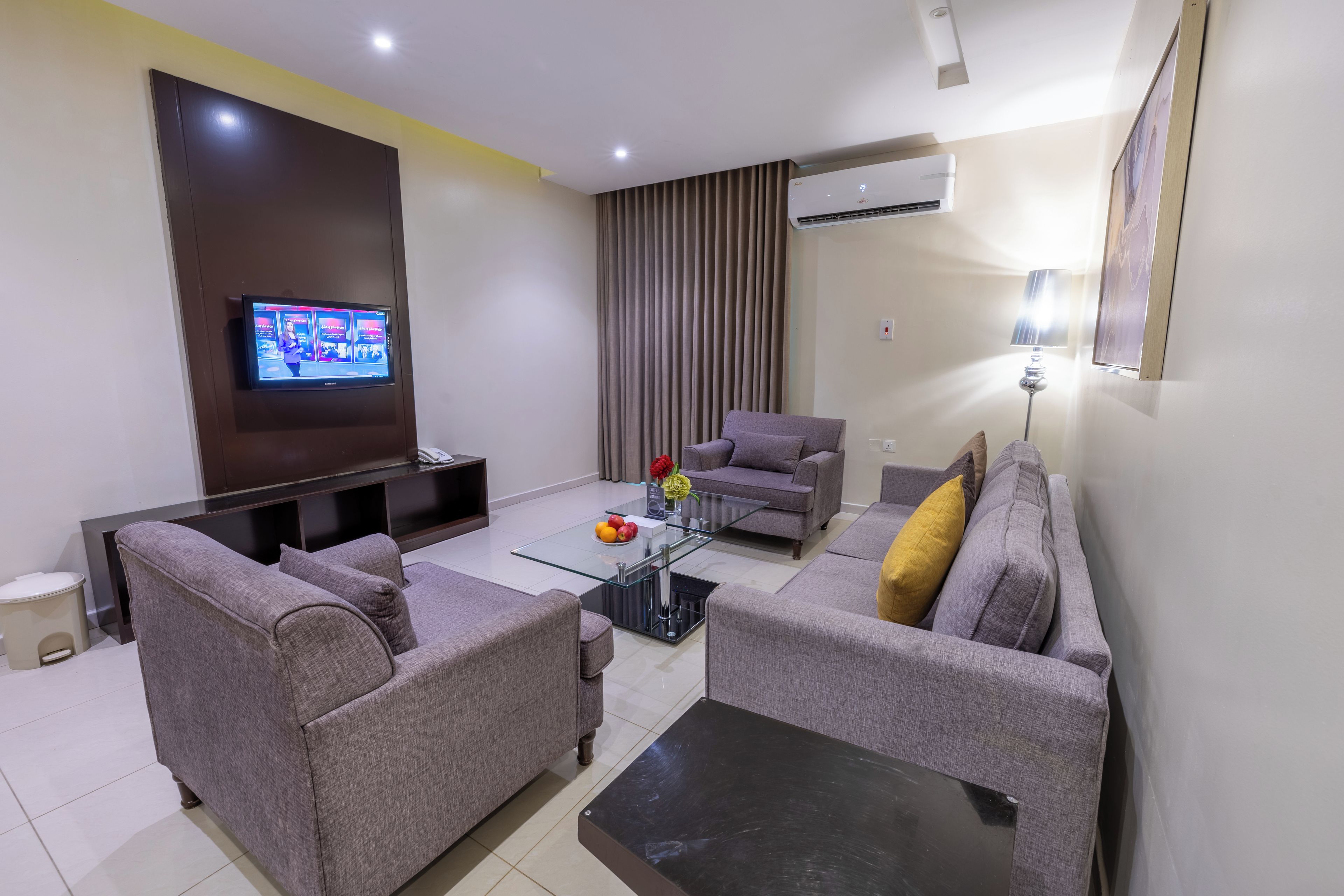 A modern living room with a flat-screen TV, grey sofas, a coffee table, and an air conditioning unit.