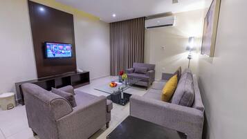 A modern living room with a flat-screen TV, grey sofas, a coffee table, and an air conditioning unit.