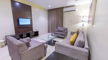 A modern living room with a flat-screen TV, two grey sofas, a glass coffee table, and an air conditioning unit.