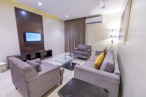A modern living room with a flat-screen TV, two grey sofas, a glass coffee table, and an air conditioning unit.