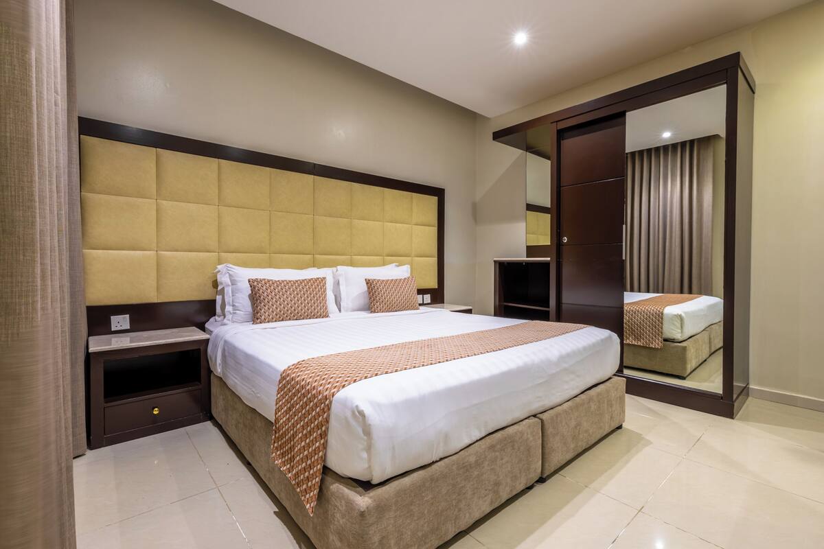 A hotel room with a large bed, a nightstand, a wardrobe, and a mirror.