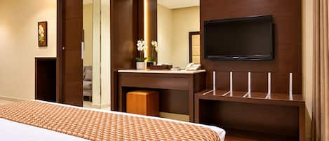 Habitación de hotel con una cama grande, un televisor montado en la pared, un escritorio con teléfono y un espejo.