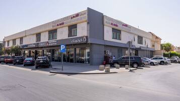 Un edificio de varios pisos con locales comerciales en la planta baja, que incluyen un letrero de estacionamiento y escaparates.