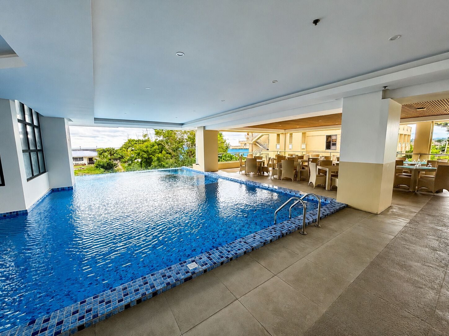 Una amplia piscina cubierta con borde de azulejos, rodeada por un área de comedor con mesas y sillas.