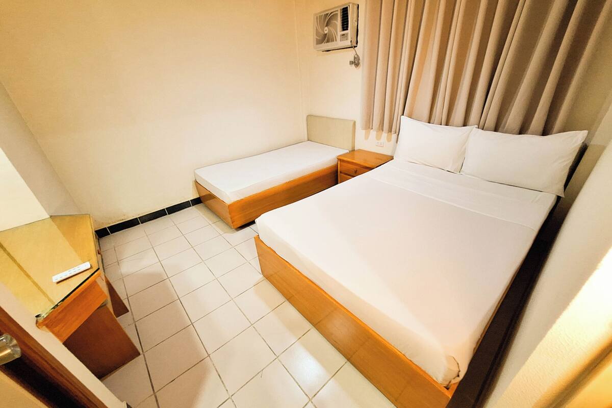 Ein Hotelzimmer mit einem großen Bett, einem kleineren Bett, einem Nachttisch und einer Wand-Klimaanlage.
