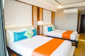 Zwei nebeneinanderliegende Hotelbetten mit weißer und orangefarbener Bettwäsche, eine Wand-Klimaanlage und ein Nachttisch mit Lampe.
