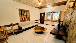 A room with a wooden bench, a sofa, a round wooden table, and a stone wall.