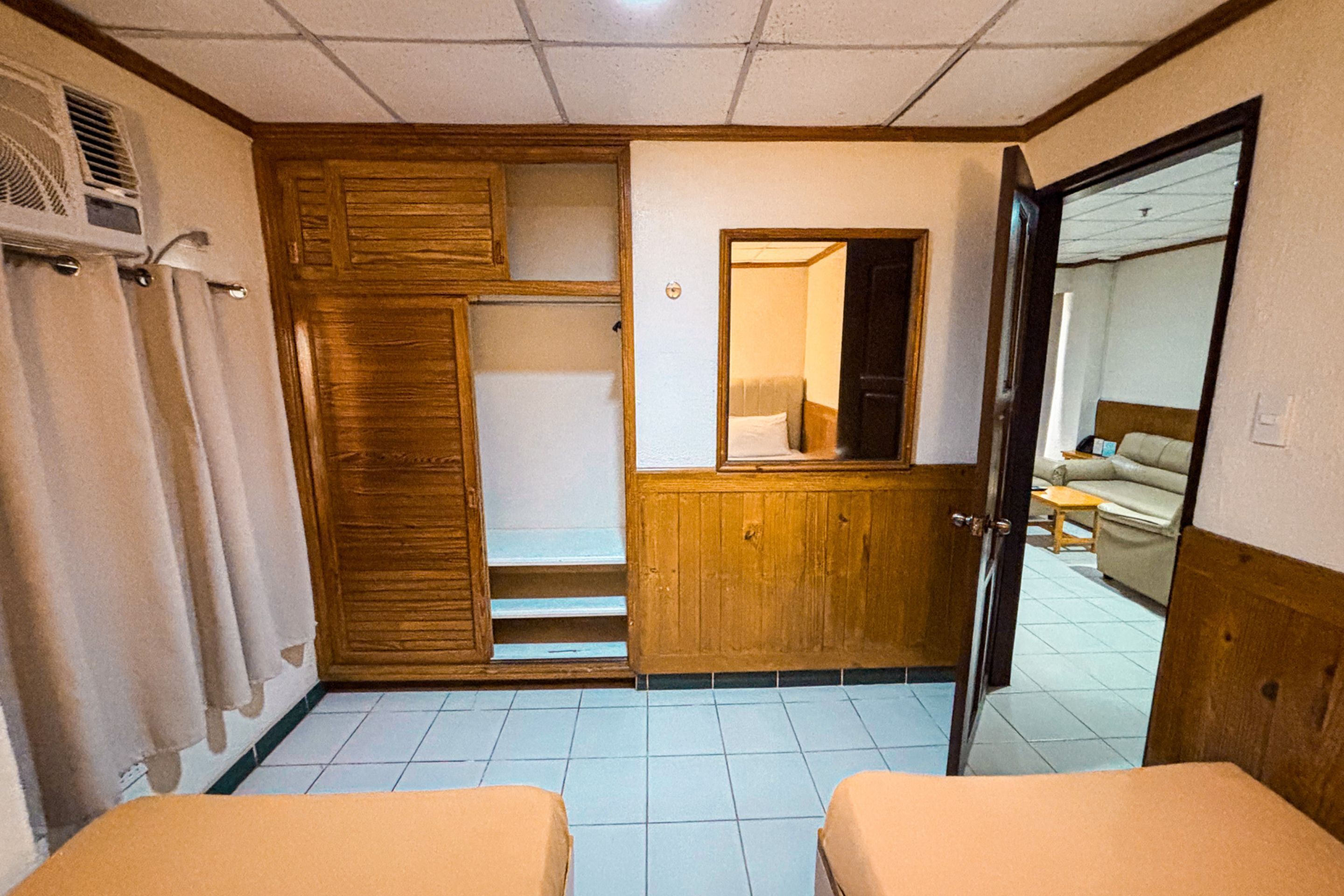Une chambre d’hôtel avec une armoire en bois, un petit bureau, un miroir et un lit.