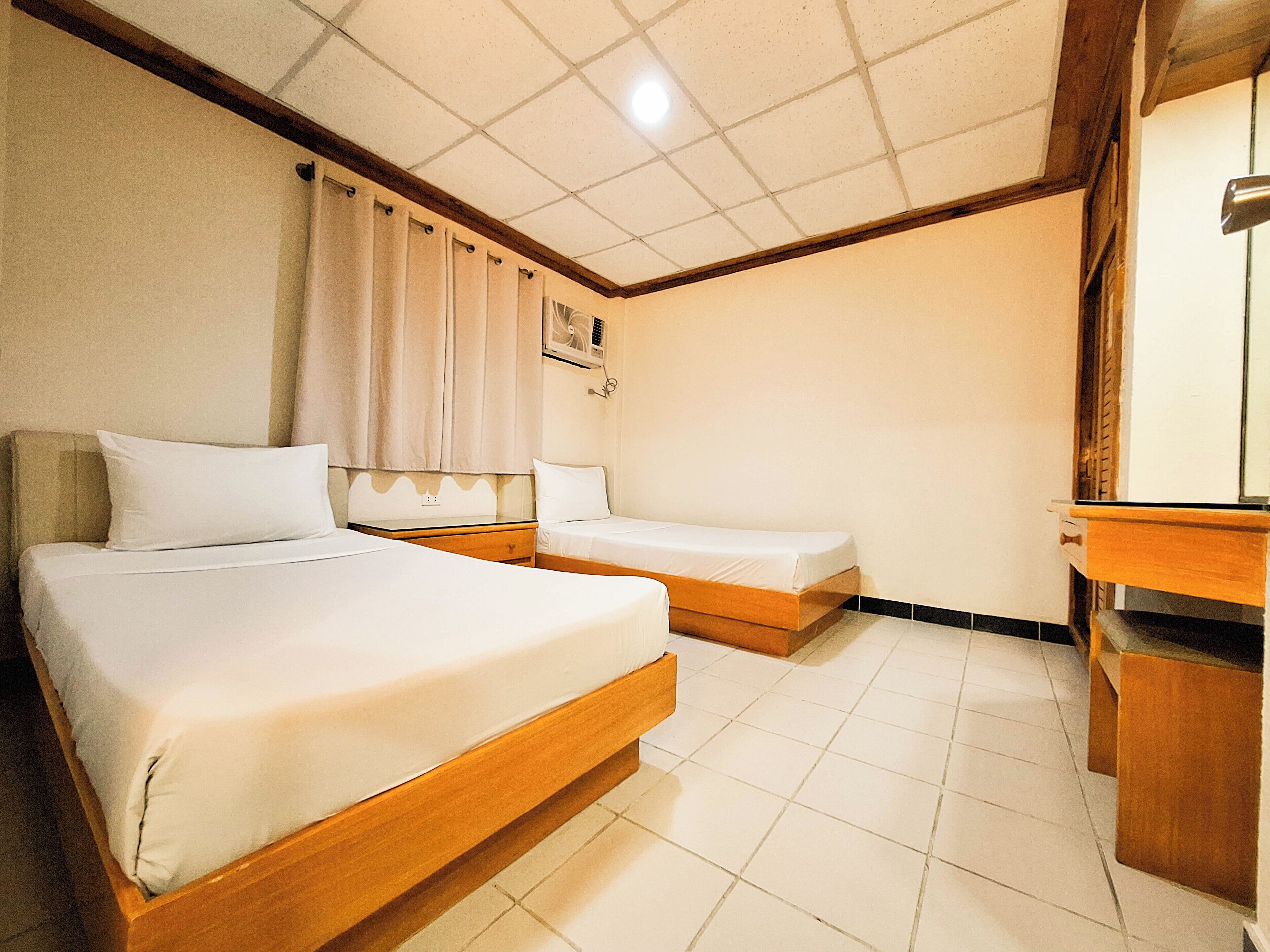 A hotel room with two single beds, a wooden headboard, a small desk, and a mirror.