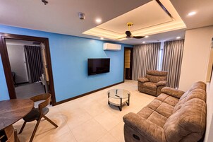 Una sala de estar moderna con un sofá, un televisor montado en la pared, un ventilador de techo y un comedor con mesa y sillas.