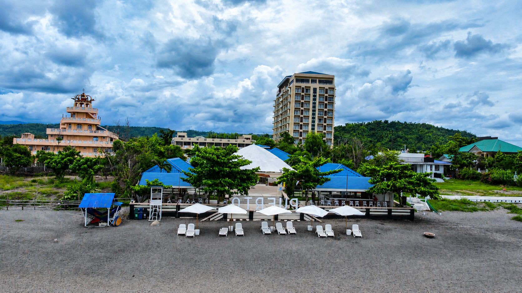 Un resort con un edificio grande, una pagoda y una zona de playa con sillas y sombrillas.