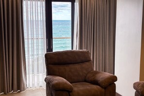 A room with a view of the sea through sheer curtains, a brown leather armchair, and a white wall. - Puerto de San Juan Beach Resort Hotel and Residences La Union (San Juan)