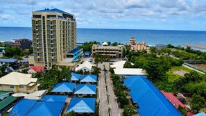 A coastal hotel with multiple buildings, including a prominent tower, and a parking area with blue-roofed structures. - Puerto de San Juan Beach Resort Hotel and Residences La Union (San Juan)