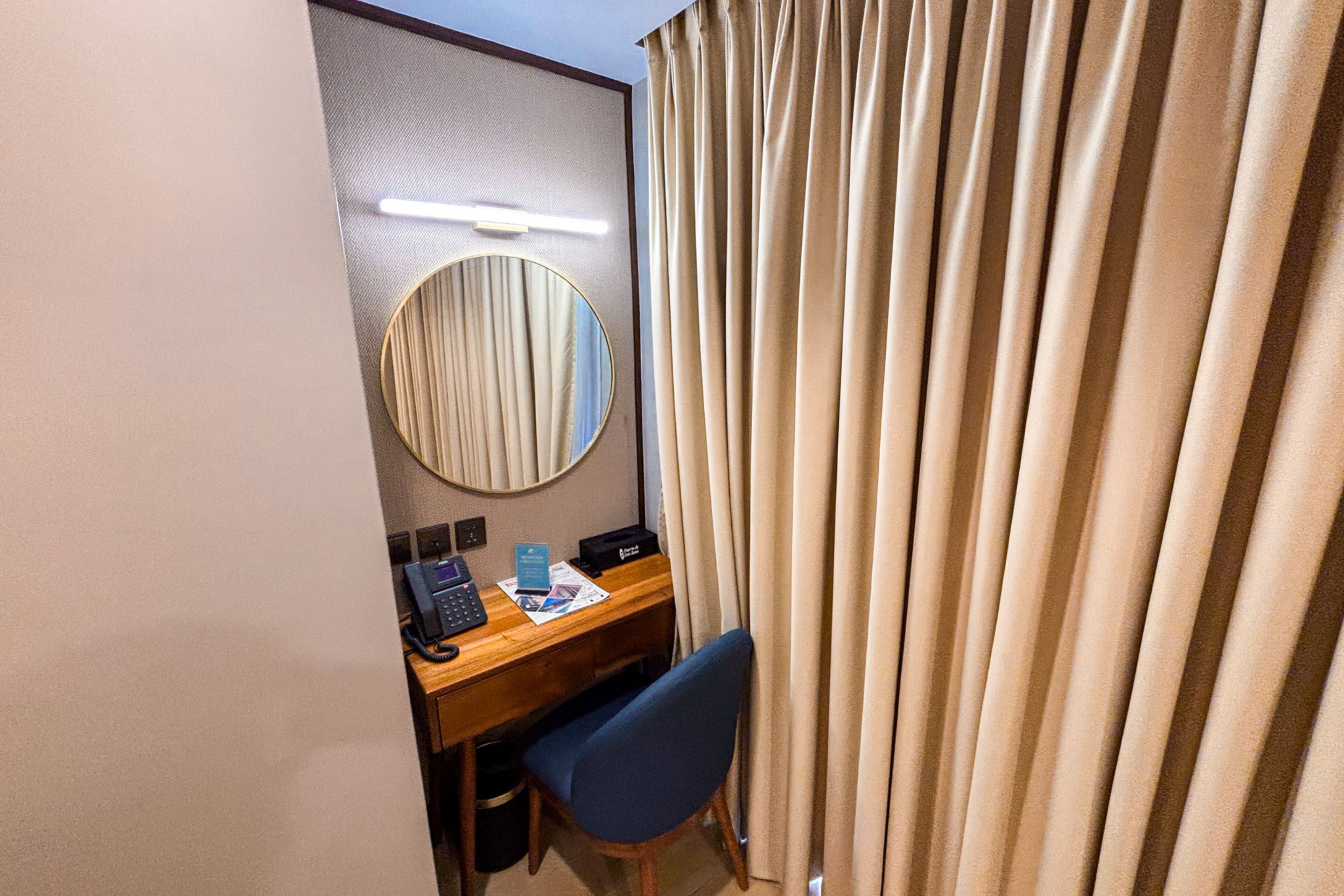 A hotel room with a desk, chair, telephone, and a mirror.