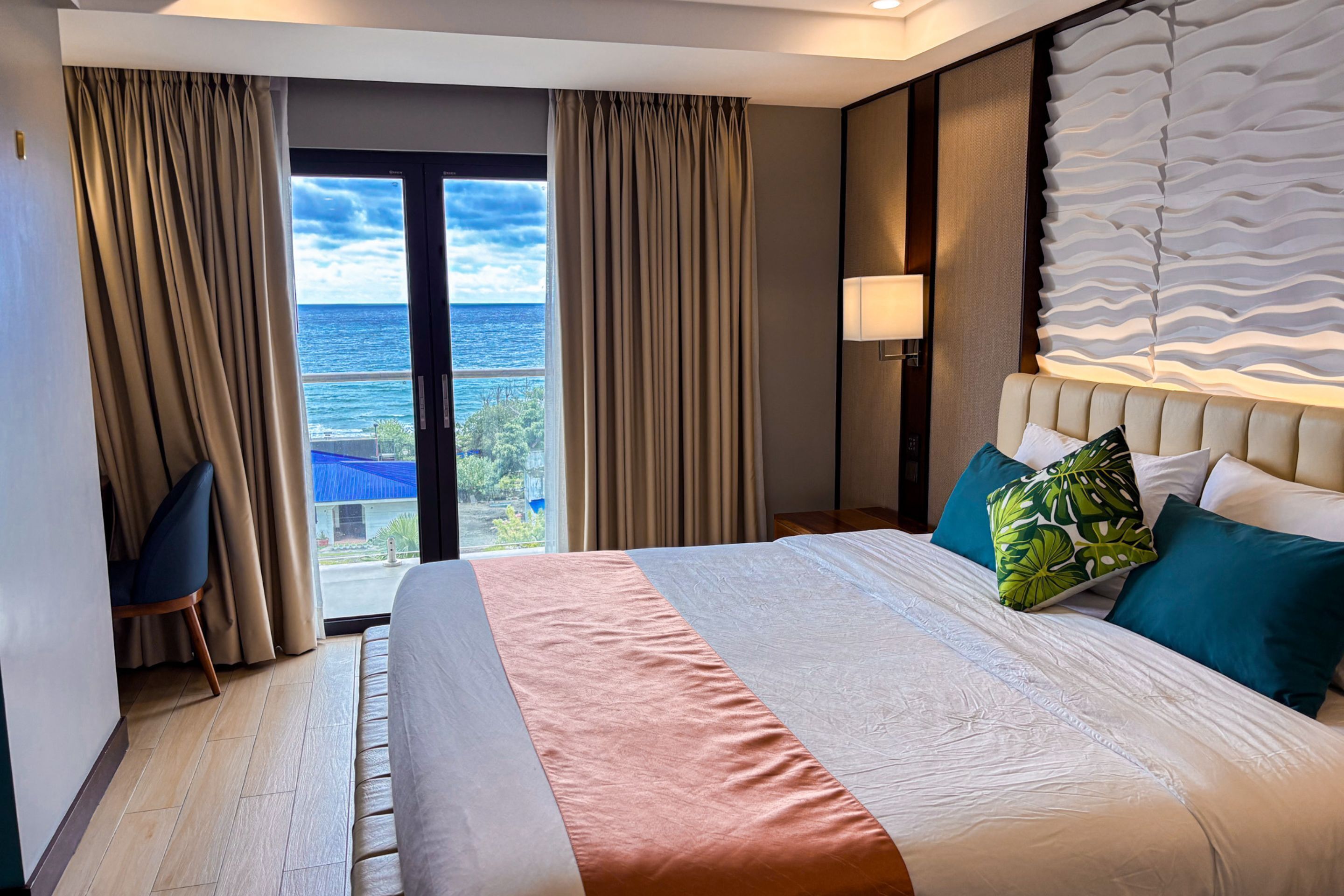 Habitación de hotel con una cama grande, vista al océano y un balcón.