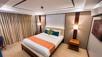 Habitación de hotel con una cama grande, dos mesitas de noche, cabecera con diseño texturizado, lámpara de pared y ventana con cortinas.