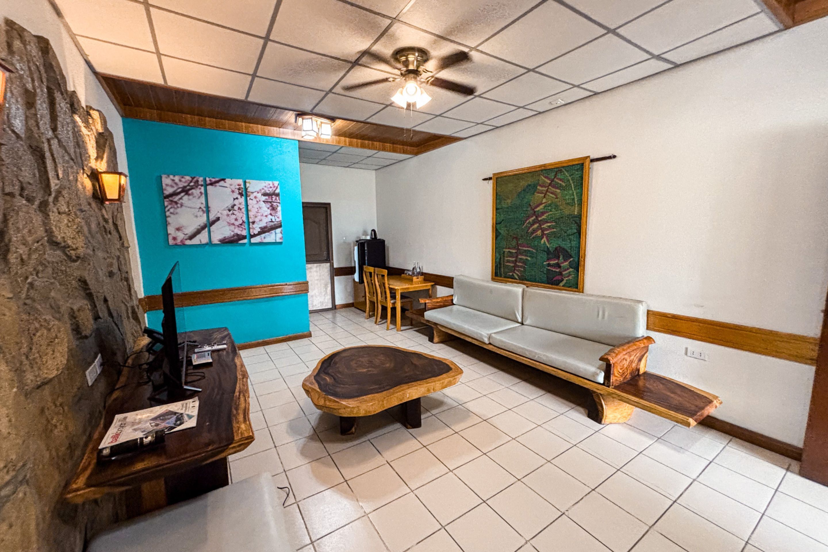 Um quarto com uma parede azul de destaque, uma mesa de centro de madeira, um sofá branco e um quadro na parede.