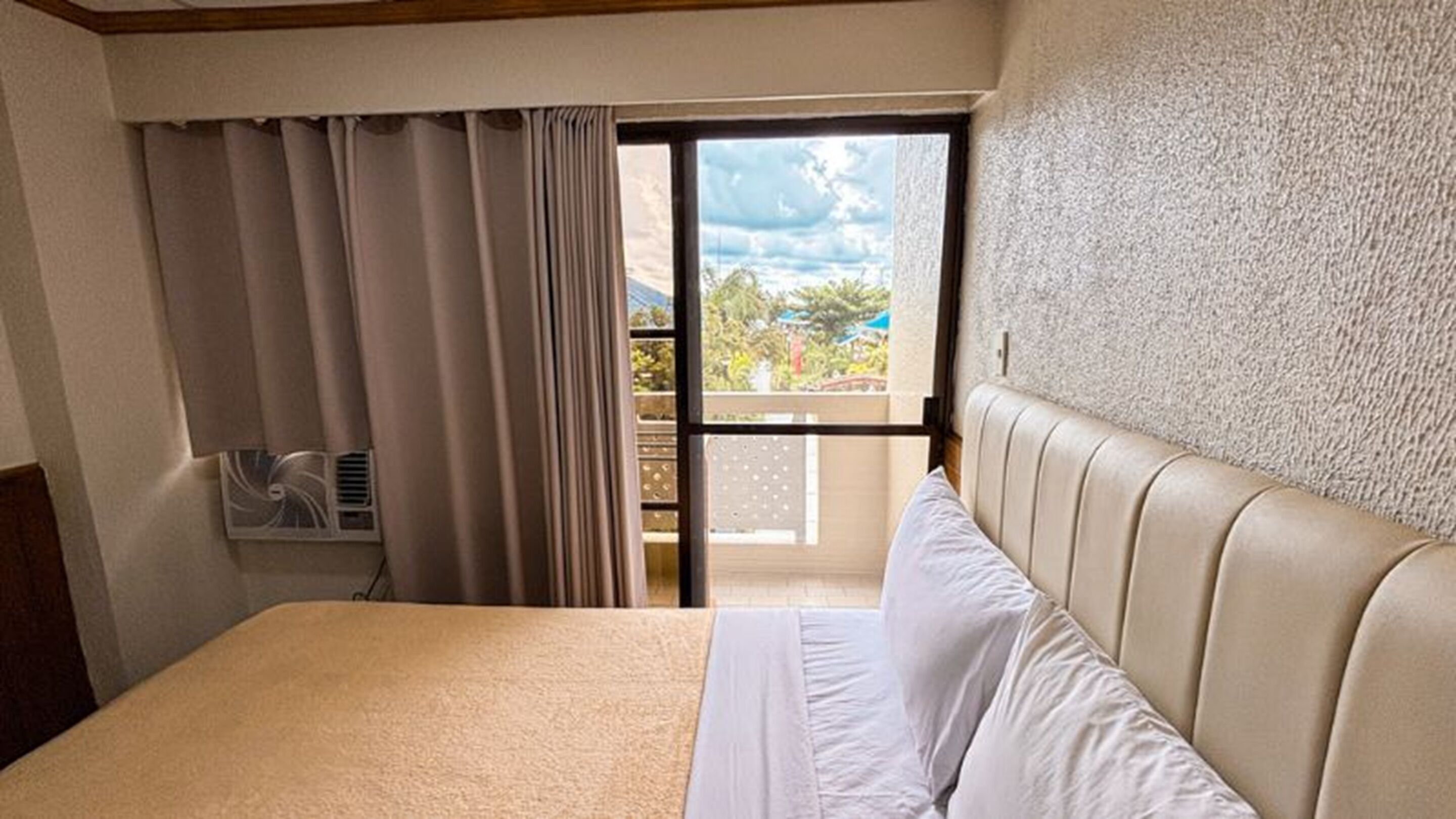 A hotel room with a bed, a window with curtains, and a view of the outdoors.