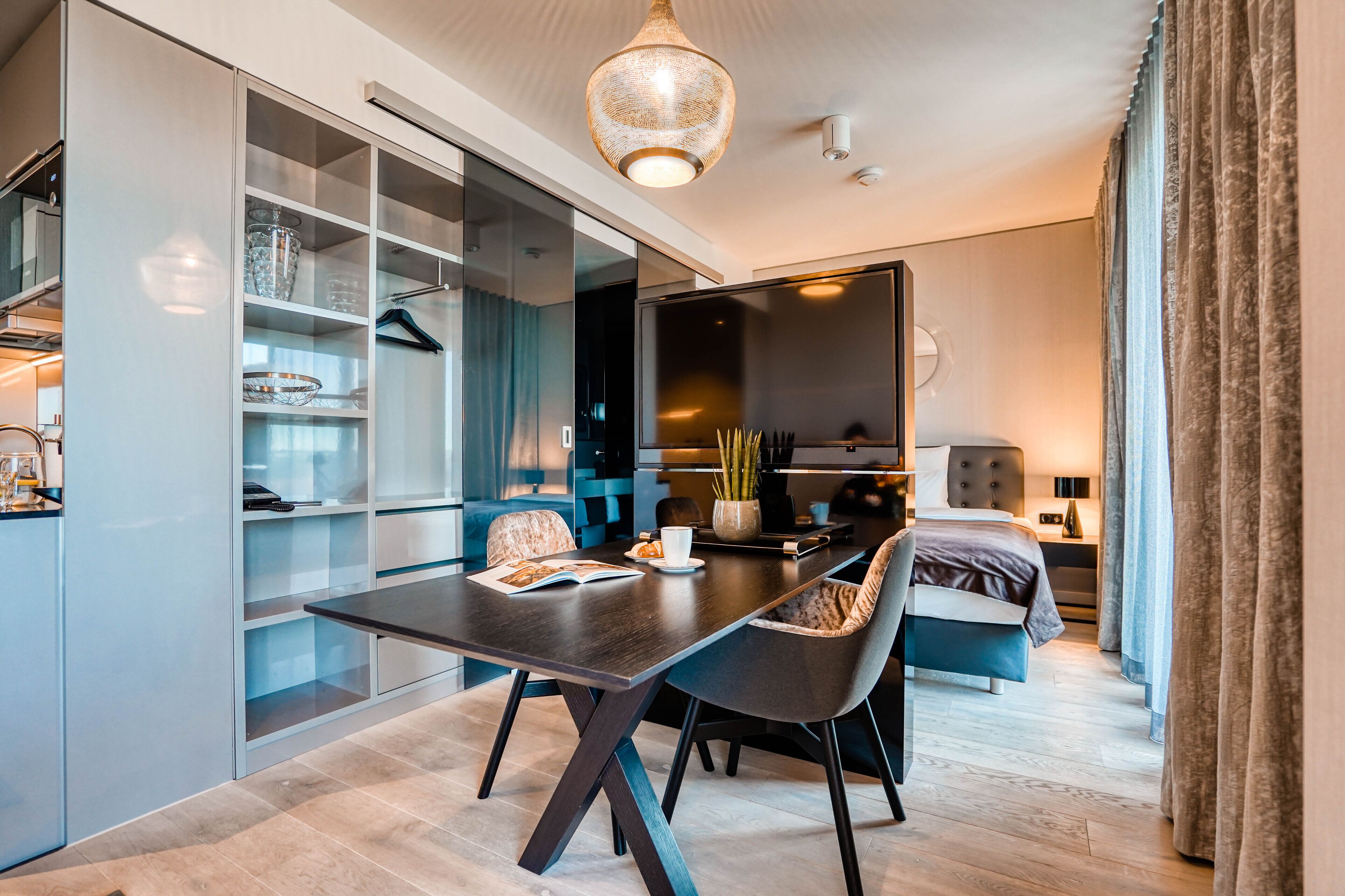 A modern hotel room with a dining area, a bed, and a large mirror.