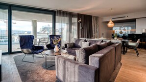 A modern living room with a large sectional sofa, a blue chair, and a dining area with a table and chairs. - CLOUD No7 Apartments (Stuttgart)