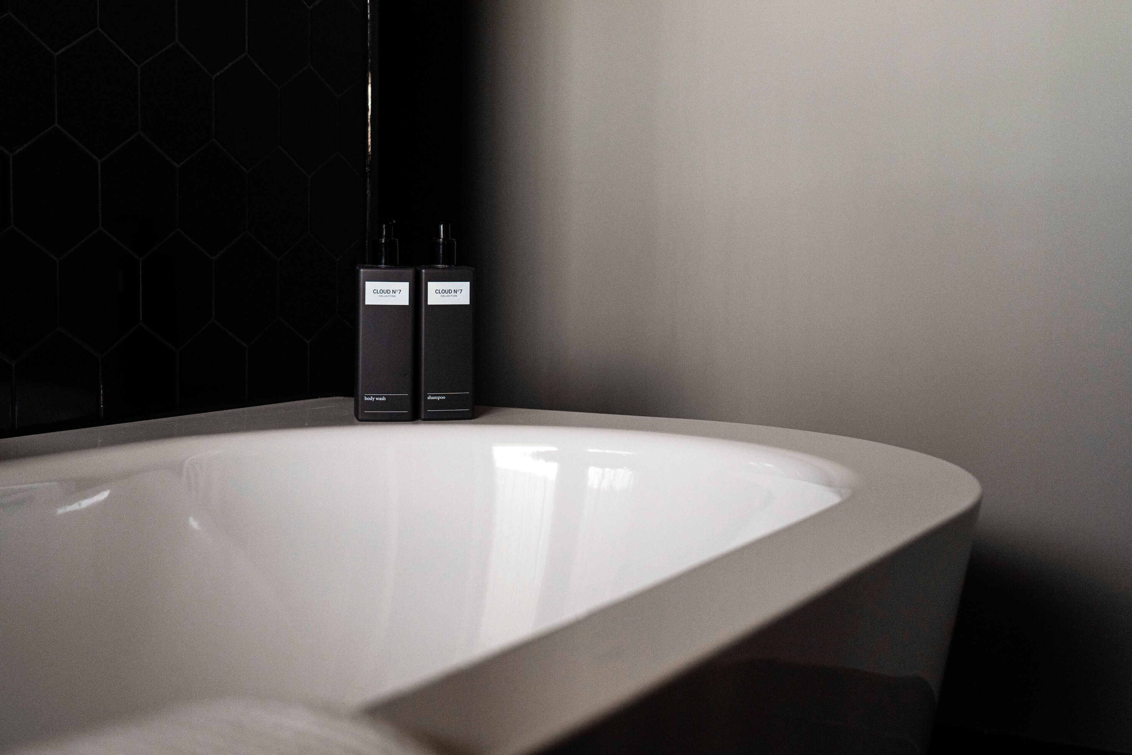 Een moderne badkamer met een groot, wit bad, twee zwarte flessen met de aanduiding 'Cloud N1' en 'Cloud N2', en een wand met een honingraatpatroon.
