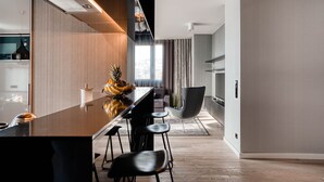 A modern kitchen with a central island, bar stools, and a dining area with a chair. - CLOUD No7 Apartments (Stuttgart)