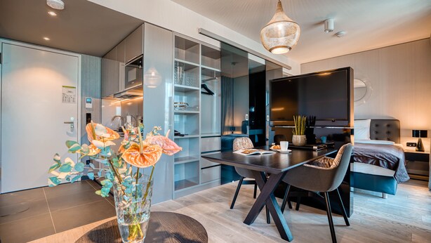 A modern hotel room with a dining area, a TV, and a bed. - CLOUD No7 Apartments (Stuttgart)