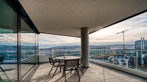 A modern balcony with a glass table and chairs, offering a city view. - CLOUD No7 Apartments (Stuttgart)