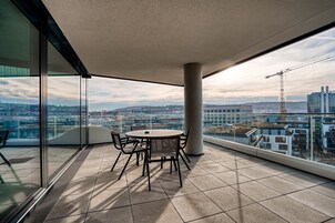Un balcón moderno con una mesa y sillas de vidrio, con vistas a la ciudad.