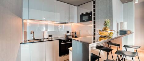 A modern kitchen with white cabinets, a microwave, a sink, and a bar area with stools.