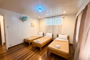 A hotel room with three single beds, a ceiling fan, a window with curtains, and a wooden floor.