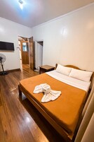 A hotel room with a bed, a bedside table, a fan, and a television.