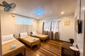 A hotel room with two single beds, a small table with a plate and a glass, a ceiling fan, and a TV mounted on the wall. - Villa Silvina Hotel and Restaurant Baguio City (Baguio)