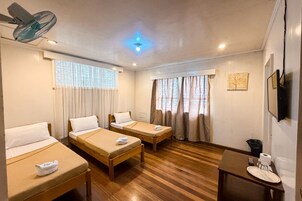A hotel room with two single beds, a small table with a plate and a glass, a ceiling fan, and a TV mounted on the wall.